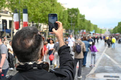 Muškarac mobilnim telefonom snima ljude na ulici. Čovjek snima pametnim telefonom ljude u gradu Parizu. Turist sa mobilnim telefonom snima fotografije.