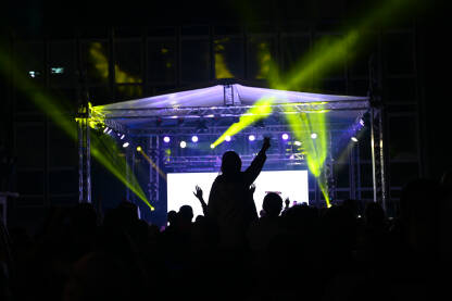 Publika ispred bine na festivalu. Ljubitelji muzike na rock koncertu. Rasvjeta i osvjetljenje pozornice tokom muzičkog koncerta.