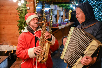 Ulični svirači u Rumuniji. Ljudi pjevaju i sviraju na sajmu. Čovjek u kostimu Djeda Mraza svira saksofon.