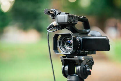 Krupni plan profesionalne video kamere sa zelenkastom zamagljenom pozadinom. Snimanje događaja na terenu video kamerom.