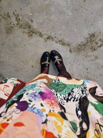 Žena u modernoj lepršavoj haljini veselog printa posmatra svoje crne lakovane cipelice.