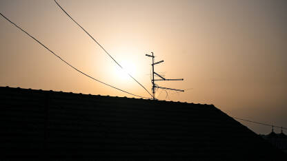 TV antena i kablovi na krovu kuće tokom zalaska sunca.