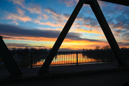Vožnja autom preko mosta preko rijeke tokom zalaska sunca. Narandžasti zalazak sunca na horizontu. Rijeka Sava.