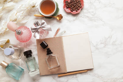 Bočice raznih parfema sa notesom olovkom i testerima na stolu uz čaj i zrna kafe za neutralisanje mirisa.