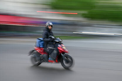 Čovjek se brzo kreće na motociklu na ulici. Vožnja skuterom po gradu. Vozač motocikla. Blurana fotografija.