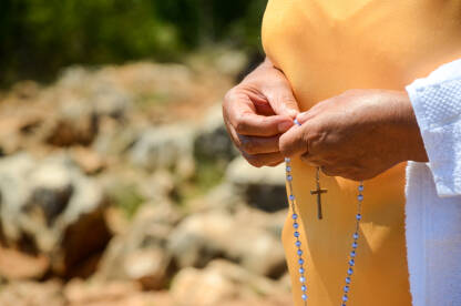 Žena vjernica drži krunicu u ruci. Molitva. Kršćanka se moli Bogu.
