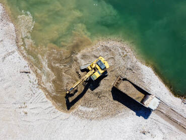 Bager kopa i utovaruje pijesak u kamion na obali rijeke. Teški strojevi rade u kamenolomu pijeska. Snimak dronom na bager i kamion koji utovaruju šljunak u prirodi. Zagađenje okoliša i vode