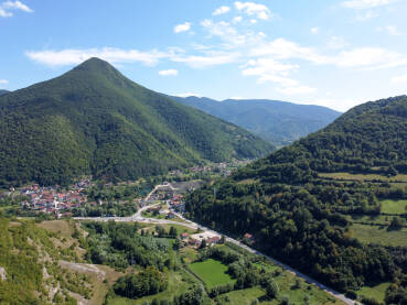 Visoko brdo sa šumom iznad sela. Naselje u dolini, snimljeno dronom. Jezero, Bosna i Hercegovina.