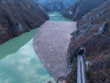 Razni oblici komunalnog otpada nagomilani u rijeci Drini, vidljivi na površini i uz obalu.