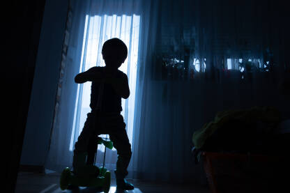 Silueta dječaka koji se igra svojim romobilom u sobi