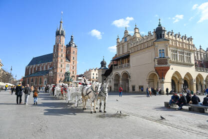 Krakow, Poljska. Kočije na glavnom trgu ili Rynek Glówny. Bazilika sv. Marije. Ljudi na trgu.