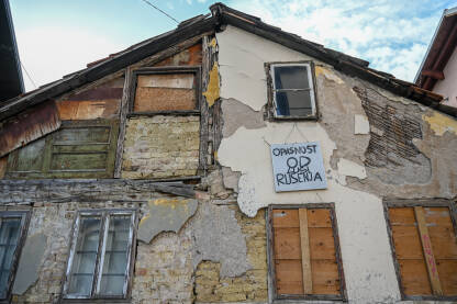 Stara oronula kuća. Kuća koja se urušava. Natpis na tabli: Opasnost od rušenja.