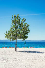 Šljunčana plaža sa suncobranima, ležaljkama i pogledom na ostrva Hvar i Brač.