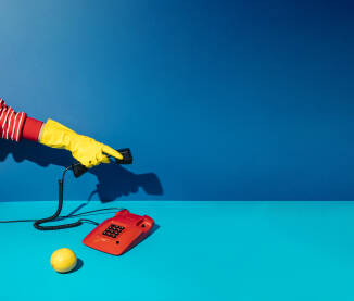 Minimalan retro koncept s rukom u žutoj rukavici za čišćenje koja podiže slušalicu crvenog telefona na plavoj pozadini.