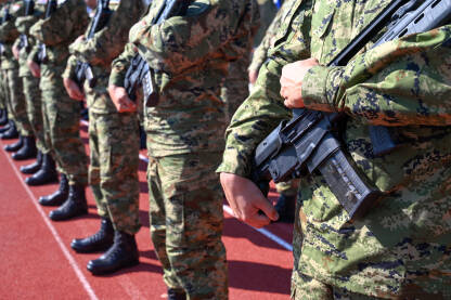 Vojnici stoje u formaciji držeći puške u kasarni. Vojna parada s naoružanim vojnicima u uniformama. Grupa vojnika drži automatske puške.