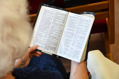 Starija žena moli u crkvi. Žena drži knjigu tokom molitve. Vjernici se mole.