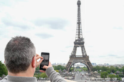 Pariz, Francuska: Turisti fotografišu Eiffelov toranj. Muškarac fotografiše Pariz svojim pametnim telefonom. Popularna turistička destinacija.