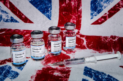 Cijepljenje protiv Covid-19. Bočica s cjepivom i šprica sa zastavom Ujedinjenog kraljevstva u pozadini. Imunizacija. Pandemija korona virusa.  Zastava Velike Britanije.