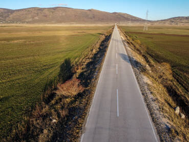 Snimak dronom na dugu ravnu cestu u polju. Asfaltna cesta u polju tokom zalaska sunca. Seoski krajolik s ravnom cestom. Kupreško polje, Kupres, Bosna i Hercegovina.