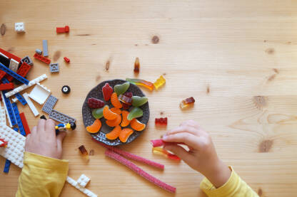Dječije ruke na stolu sa gumenim bombonama i lego kockicama.