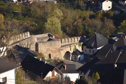 Banjalučka kapija u Jajcu u fokusu pored drugih stambenih gradskih objekata i vidljive zelene površine.