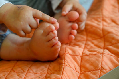 Male, dječije noge na narandžastom prekrivaču. Dijete dira bose noge.