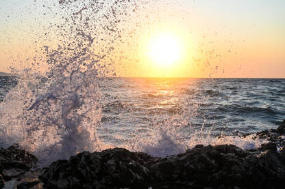 Valovi se razbijaju o kamenitu plažu tokom zalaska sunca. Talasi na moru. Jadransko more.