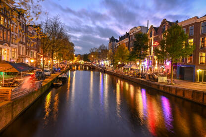 Zgrade, drveće i kanal u Amsterdamu noću. Grad Amsterdam, Holandija. Holandske kuće.