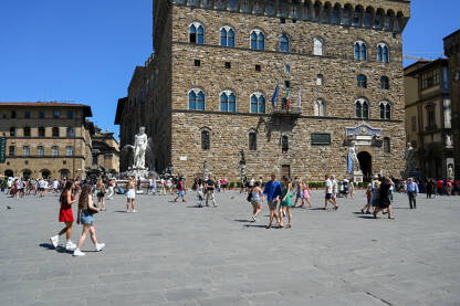 Firenca, Italija: Palazzo Vecchio, replika kipa Davida i Neptunova fontana na Piazza della Signoria. Ljudi šetaju trgom. Historijske građevine. Turisti istražuju grad.