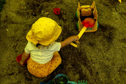 Dijete se u pijesku igra sa lopaticom i kamiončićem