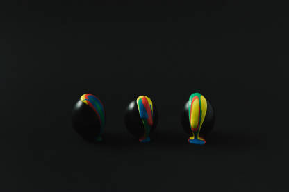 Tri crna uskršnja jaja preko kojih cure zelena, crvena, plava i žuta boja.