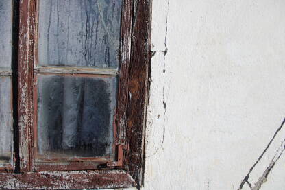 Detalj starog drvenog prozora sa puknutim zamagljenim staklom i zavjesom iza stakla