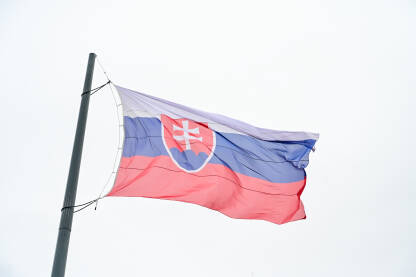 Zastava Slovačke se vijori na vjetru ispred parlamenta. Zastava Slovačke na jarbolu. Bijela, plava i crvena boja. Državni grb Slovačke.