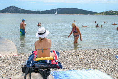 Djevojka sa šeširom se sunča na plaži. Turisti na moru. Ljetni godišnji odmor.