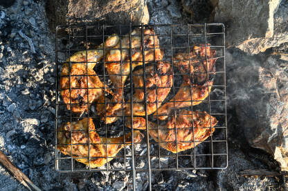 Priprema i pečenje pilećih bataka na roštilju. Pečeno pileće meso na roštilju. Ugalj i dim na pozadini. Ukusno i marinirano pileće meso na vrućem roštilju.