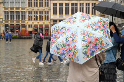 Žena drži kišobran dok pada kiša na gradskom trgu. Djevojka sa kišobranom stoji u gradu po kišovitom vremenu.