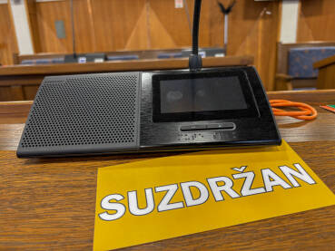 Sjednica u skupštini. Natpis SUZDRŽAN pored poslaničkog mikrofona.