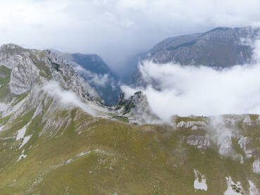 Planina u magli, snimak dronom. Oblačan dan u planinama. Litice i stijene na vrhu planinskog lanca. Oblaci prelaze planinski prijevoj. Durmitor, Crna Gora.