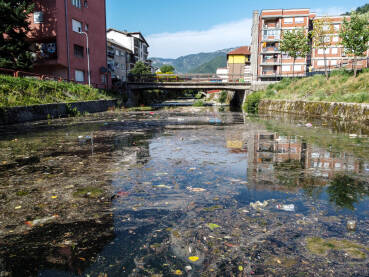 Zagađena rijeka u gradu. Smeće u rijeci. Otpad pluta u vodi. Ekološki problem. Plastične vrećice, boce i smeće bačeno u rijeku.