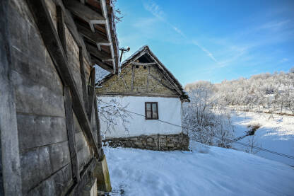 Tradicionalna seoska kuća pokrivena snijegom u selu. Stara rustikalna kuća sa kamenim temeljima i bijelim gipsanim zidovima. Balkanska arhitektura.