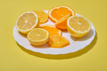 Narezani komadi narandže i limuna servirani na tanjiru na žutoj pozadini