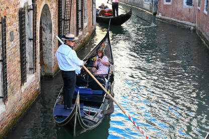Venecija, Italija: Gondola na rijeci. Istorijske građevine uz riječni kanal. Popularna turistička destinacija. Turisti istražuju grad.