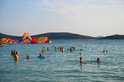 Ljudi u moru tokom turističke sezone. Prepuna plaža i more. Godišnji odmor. Turisti na odmoru na Jadranu.