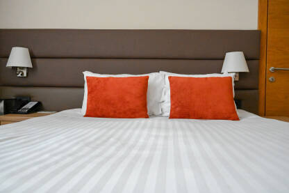 Krevet pripremljen za spavanje. Bijeli i crveni jastuci i bijeli jorgan na krevetu u hotelskoj sobi. Uredan krevet u apartmanu.