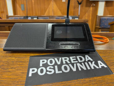 Sjednica u skupštini. Natpis POVREDA POSLOVNIKA pored poslaničkog mikrofona.