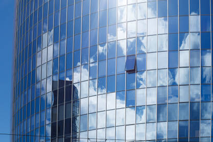 Poslovna zgrada sa staklenom fasadom Fotografija moderne staklene poslovne zgrade sa jednim otvorenim prozorom i refleksijom oblaka.Urbana arhitektura.