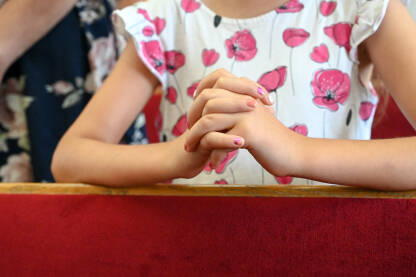 Djevojčica se moli u crkvi. Prekrštene ruke devojke tokom molitve. Sklopljene ruke, krupni plan.
