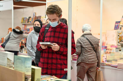 Sajam knjiga, Sarajevo. Posjetioci s maskom na licu pregledavaju knjige na sajmu knjiga. Mladić čita knjigu. Covid19.