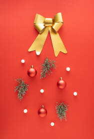 Zlatna mašna, crvene ukrasne kuglice, zelene grančice i bijele kuglice na crvenoj božićnoj, novogodišnjoj pozadini.