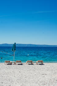Šljunčana plaža sa suncobranima, ležaljkama i pogledom na ostrva Hvar i Brač.